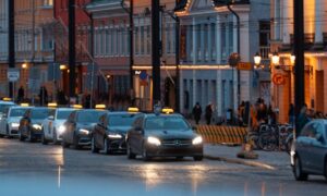 Twilight view of a historic street in Helsinki, Finland, featuring lit buildings and passing cars.